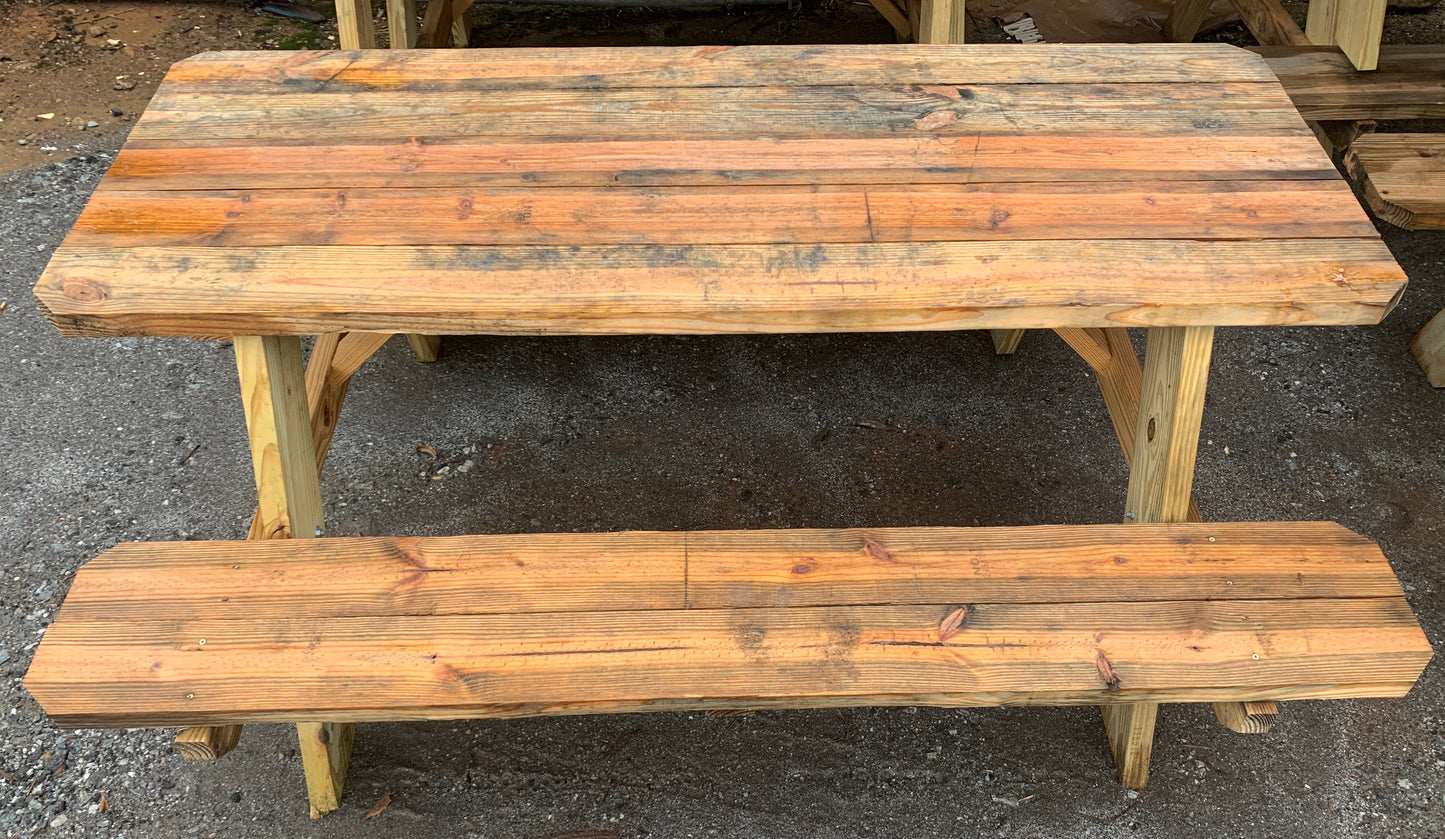 A rustic wooden picnic table with a matching bench, made from weathered reclaimed wood planks, set on a gray gravel ground.