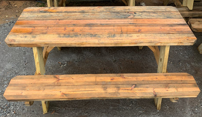 A rustic wooden picnic table with a matching bench, made from weathered reclaimed wood planks, set on a gray gravel ground.
