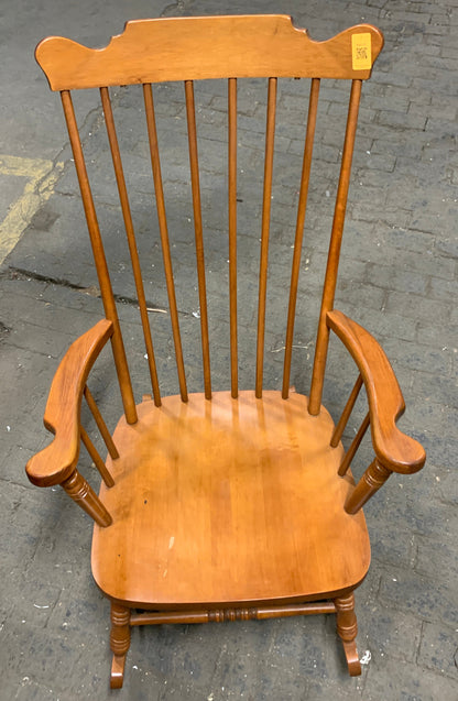 A wooden spindle-back rocking chair with a warm medium-brown finish, photographed from an overhead angle on a gray concrete floor.