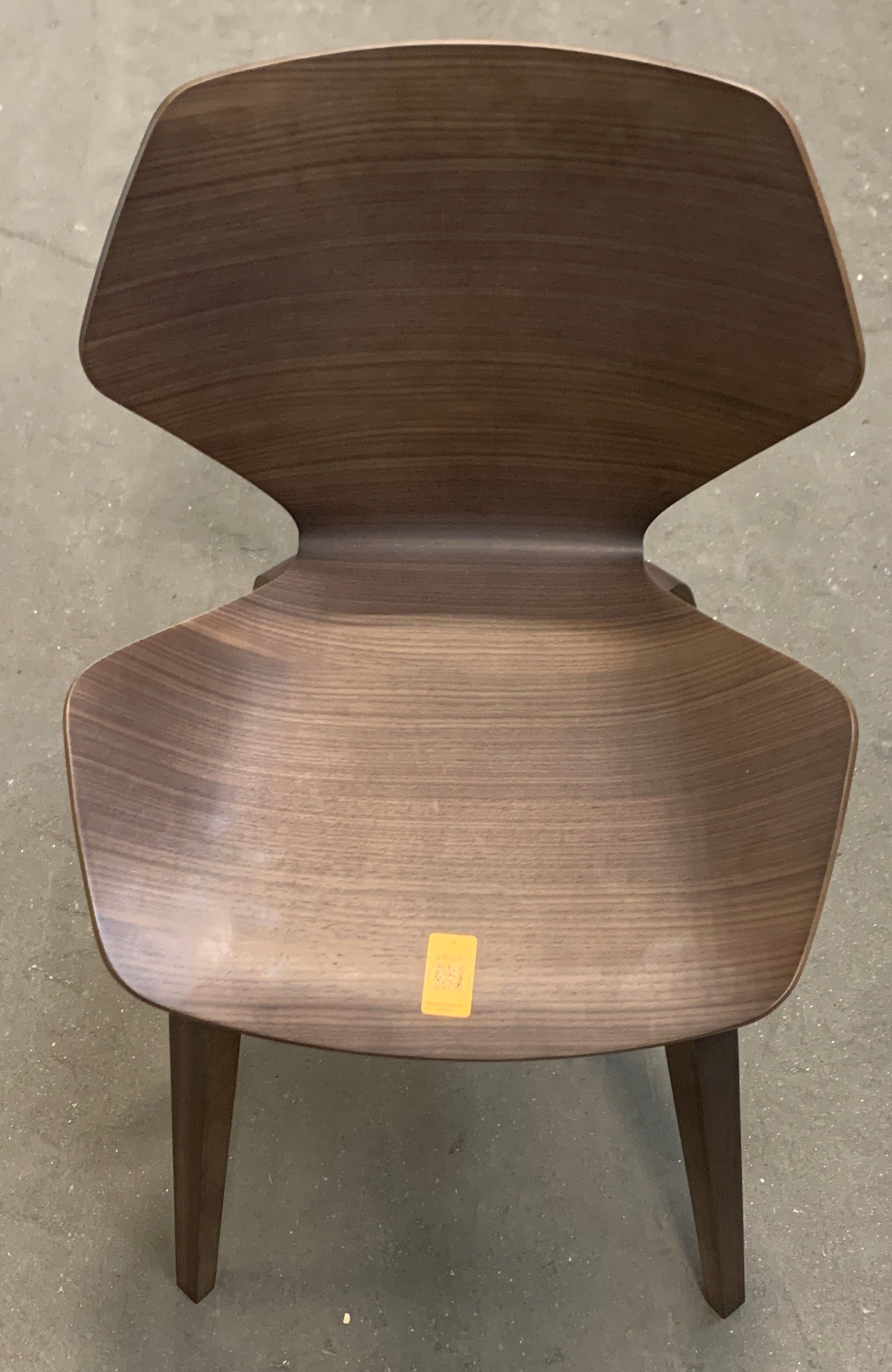 A mid-century modern wooden chair with a curved shell seat and back, shown from a top-down perspective on a concrete floor.