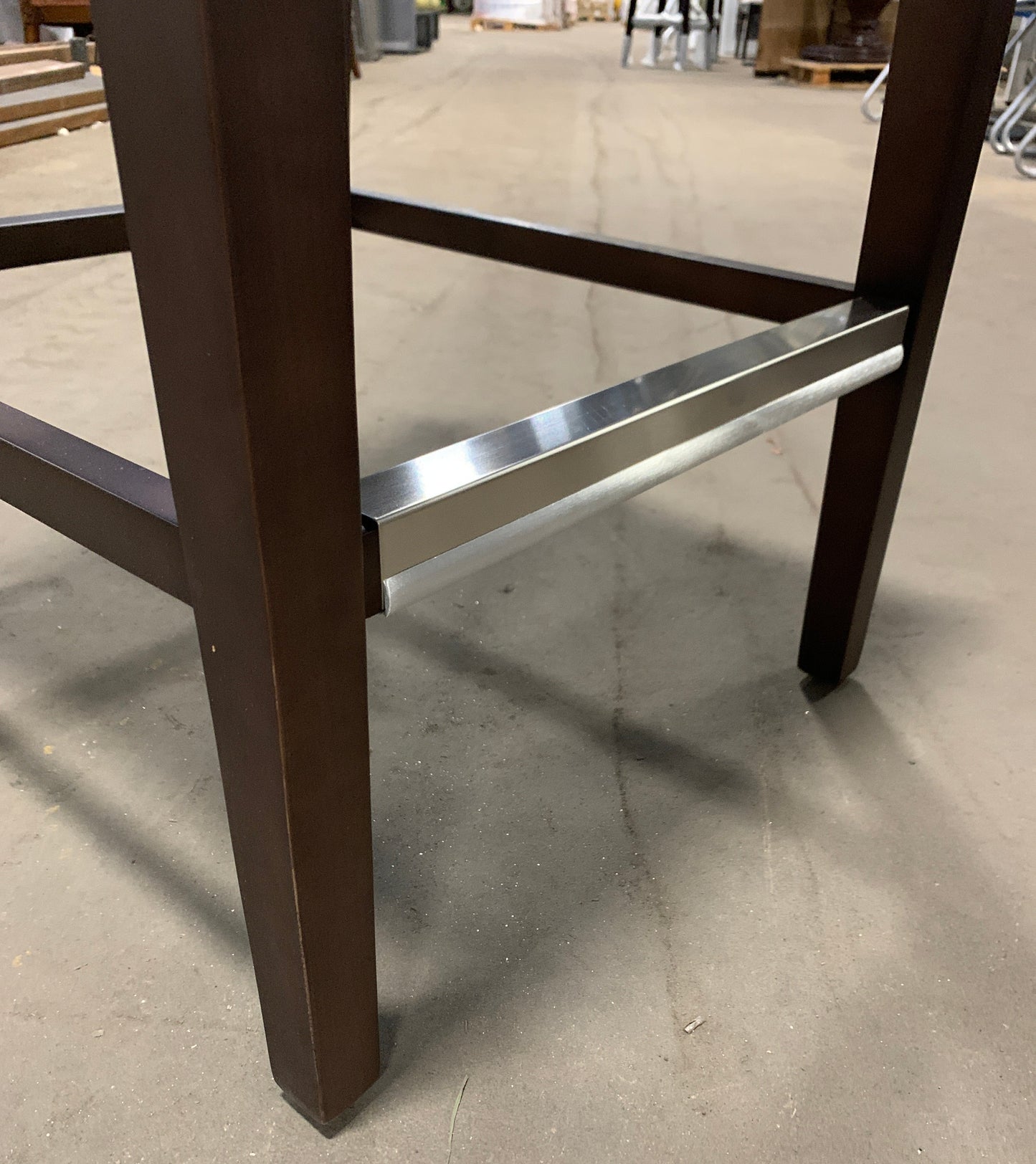 Close-up of a dark brown wooden table leg and a brushed silver metal bar support on a concrete floor.