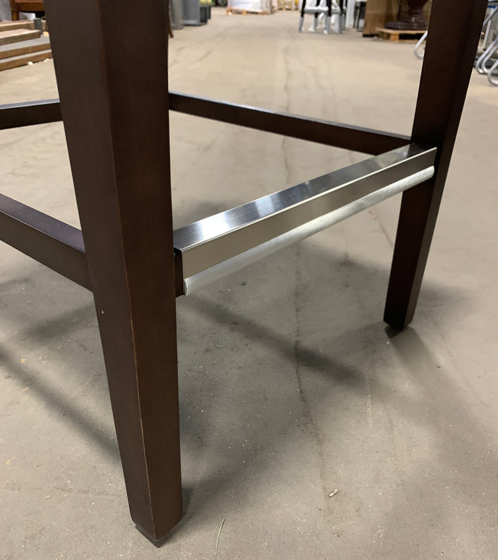 Close-up of a dark brown wooden table leg and a brushed silver metal bar support on a concrete floor.