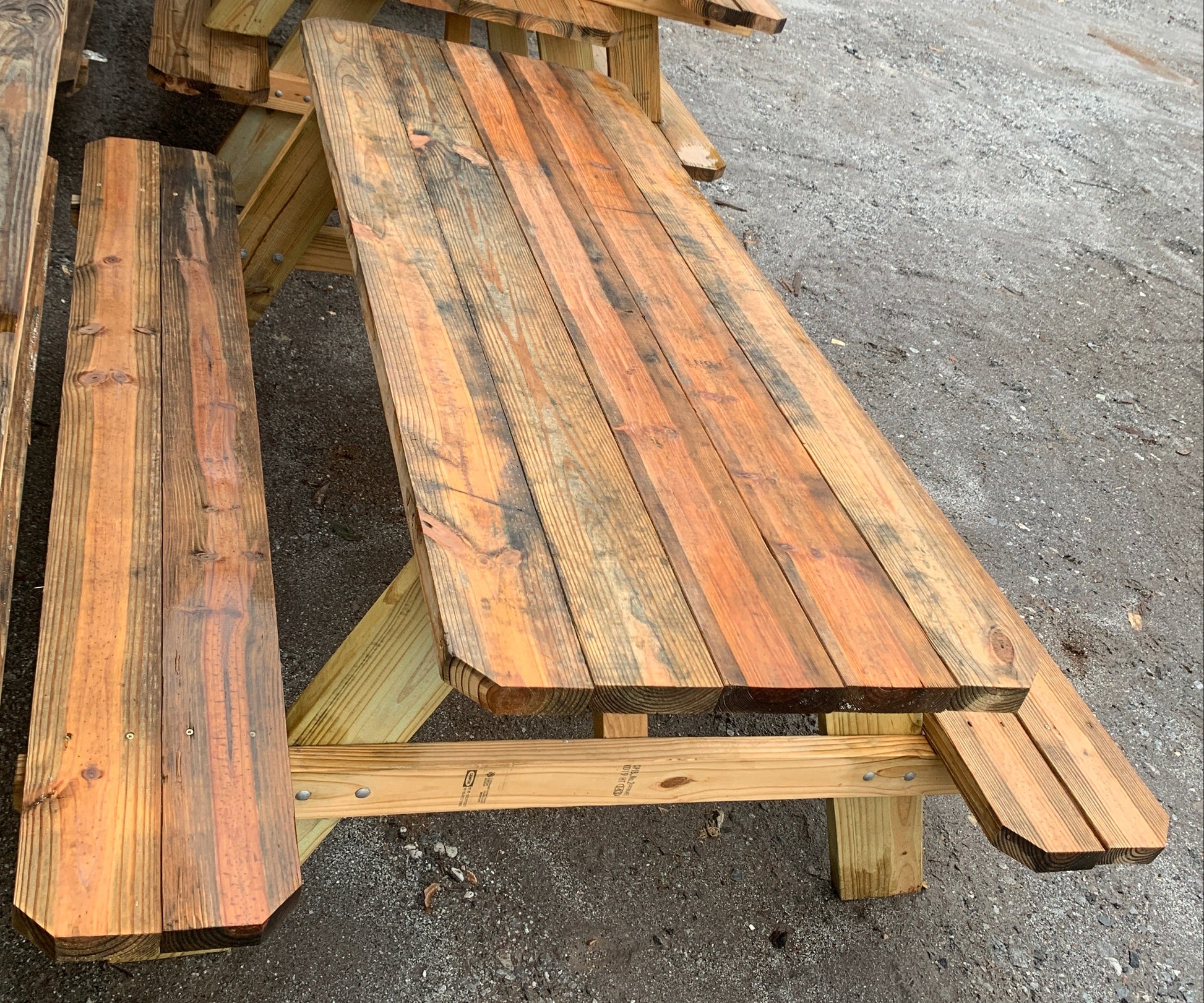 A rustic wooden Adirondack-style bench made from weathered pallet wood, photographed outdoors on a gravel surface.