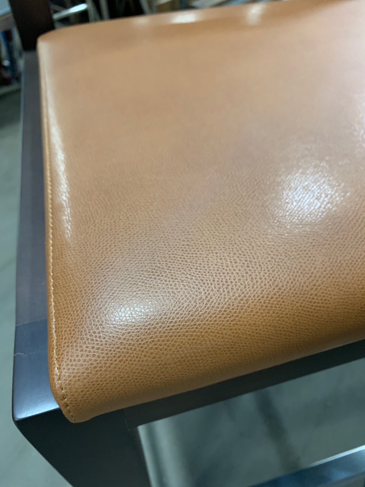 Close-up of a tan pebbled leather seat cushion on a dark metal frame, showing the texture and stitching detail.