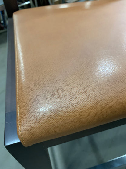 Close-up of a tan pebbled leather seat cushion on a dark metal frame, showing the texture and stitching detail.