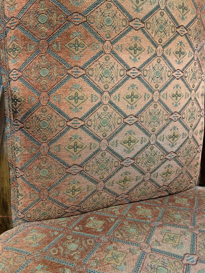 Close-up of patterned upholstery fabric on a chair or upholstered furniture piece, showing a repeating diamond motif in muted teal, rust, beige, and brown tones.