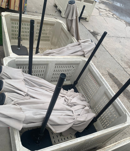 Several folded patio umbrellas with black poles and dark bases stored inside white plastic crates on a concrete surface.