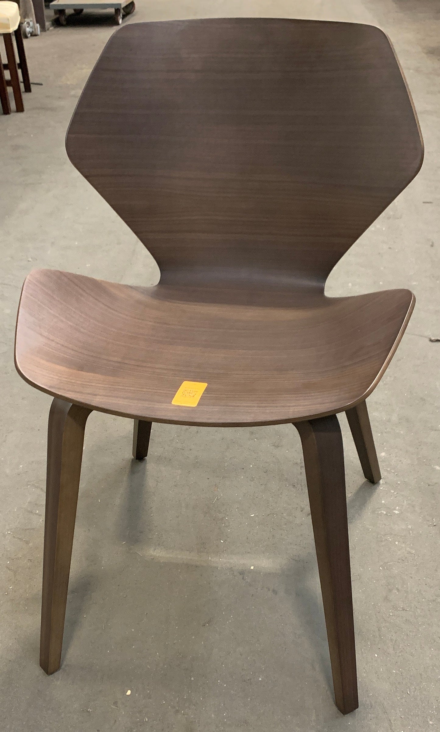 A mid-century modern wooden dining chair with a sculpted shell back and seat, shown in a furniture store on a concrete floor.
