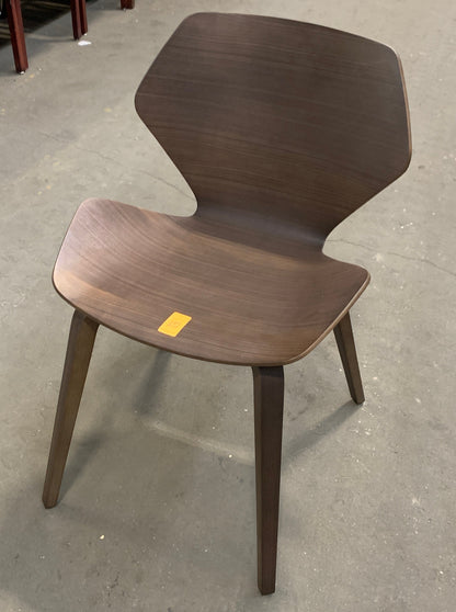 A mid-century modern wooden dining chair with a sculpted shell seat and back, shown on a concrete floor in a warehouse or furniture store.