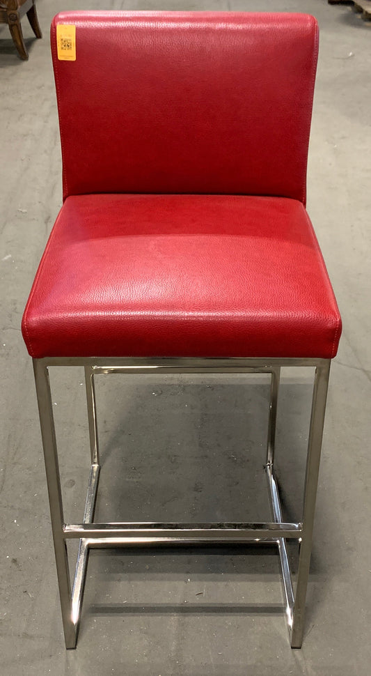 A red upholstered bar stool with a chrome metal frame, photographed in a furniture store aisle.