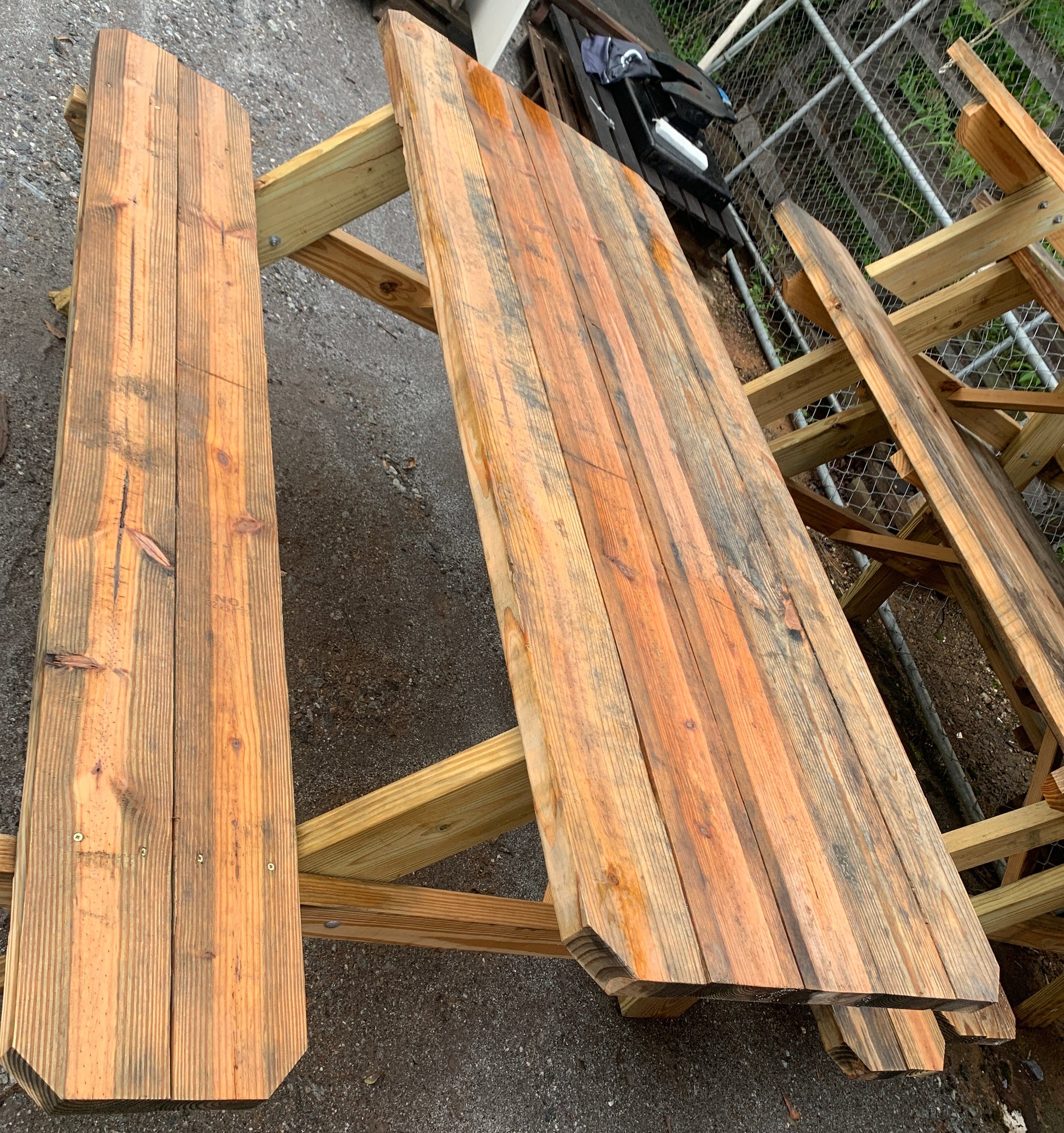 A rustic wooden picnic table with matching bench, constructed from weathered stained wood planks, photographed outdoors on a gray asphalt ground.