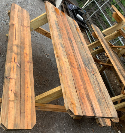 A rustic wooden picnic table with matching bench, constructed from weathered stained wood planks, photographed outdoors on a gray asphalt ground.