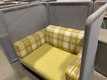 A modern gray mesh high-back lounge chair with a mustard yellow seat cushion and plaid yellow, white, and blue accent cushions, shown in a showroom setting.