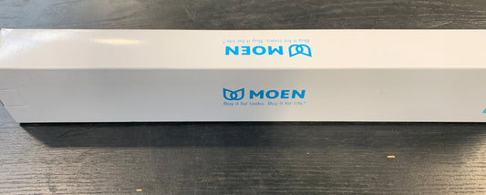 A long white MOEN product box with blue logo printing, placed horizontally on a dark wooden table.