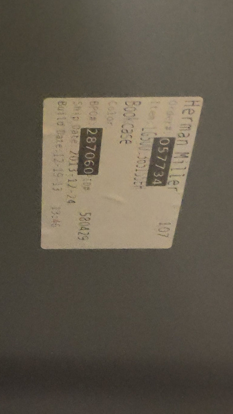 A close-up view of a dark gray metal cabinet or panel corner with a small white product label attached to the surface.