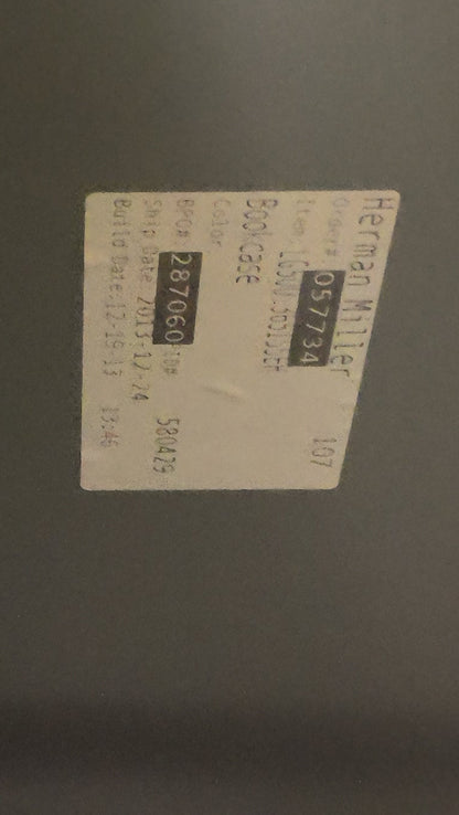 A close-up view of a dark gray metal cabinet or panel corner with a small white product label attached to the surface.